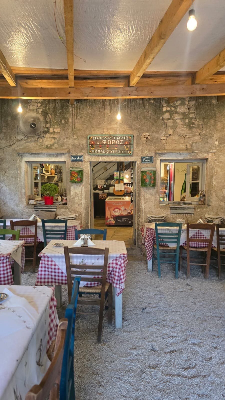 The covered courtyard of taverna O Foros with gingham tablecloths on a gravel floor